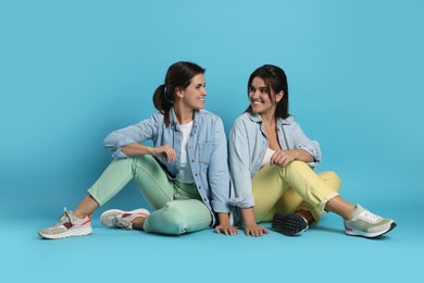 Portrait of beautiful twin sisters on light blue background