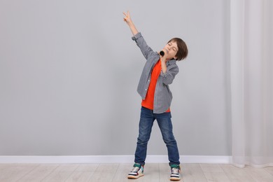 Cute boy with microphone singing near grey wall. Space for text