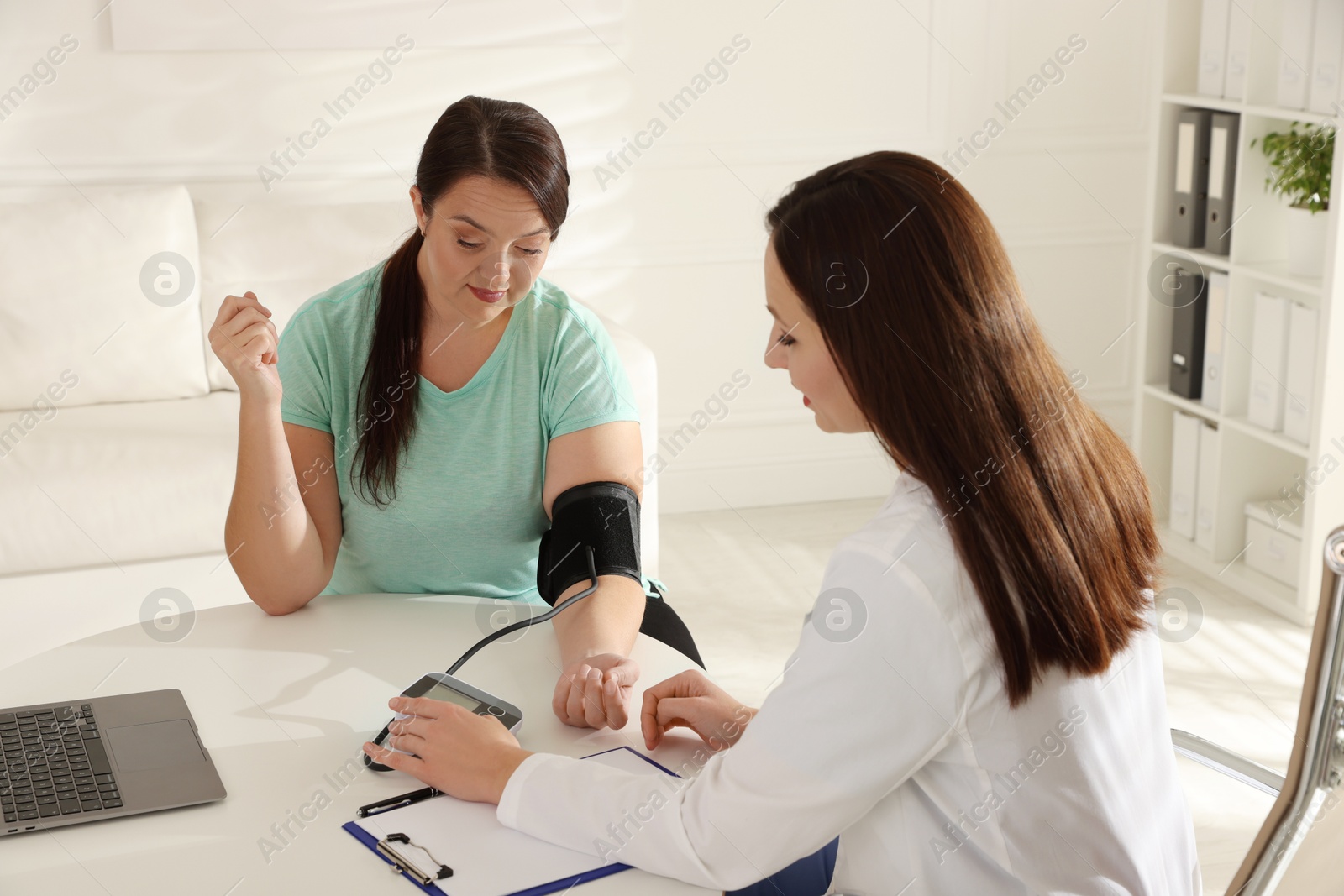 Photo of Nutritionist measuring overweight woman's blood pressure at desk in hospital