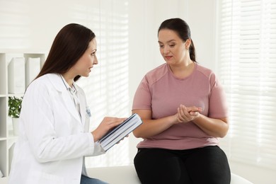 Nutritionist with notebook giving recommendations to overweight woman in hospital