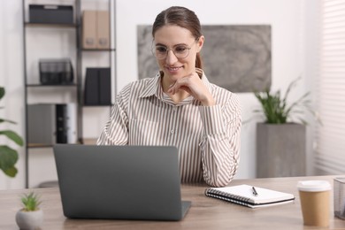 Photo of Programmer working on laptop at wooden desk indoors