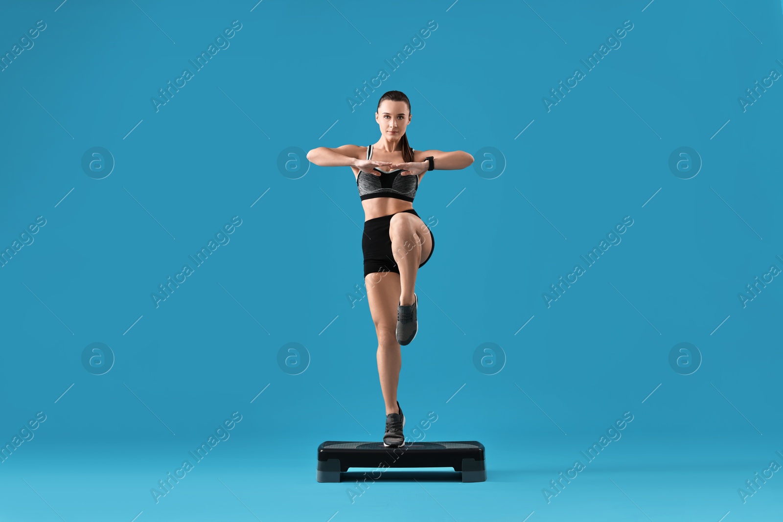 Photo of Woman in gym clothes doing exercise with step platform on light blue background