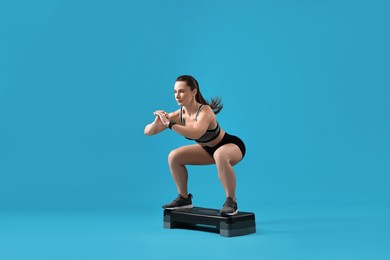 Photo of Woman in gym clothes doing exercise with step platform on light blue background, space for text