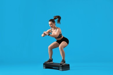 Photo of Woman in gym clothes doing exercise with step platform on light blue background, space for text