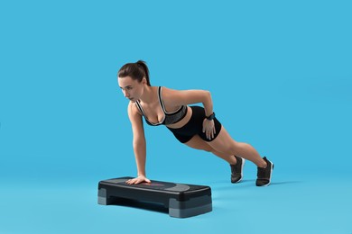 Photo of Woman in gym clothes doing exercise with step platform on light blue background