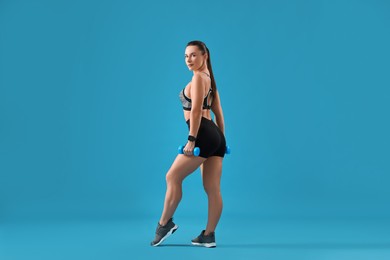 Photo of Woman in gym clothes exercising with dumbbells on light blue background