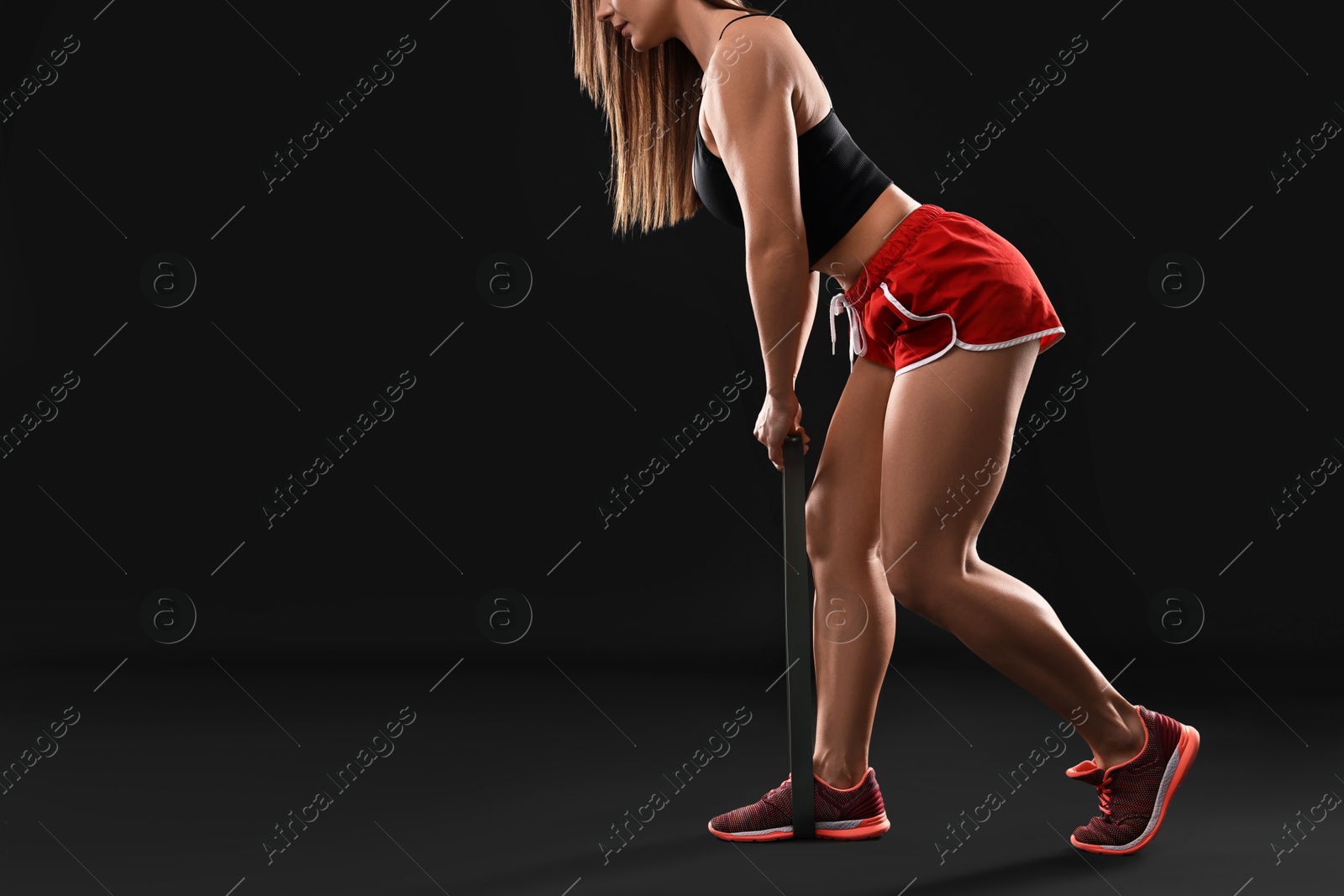 Photo of Woman in gym clothes doing exercise with elastic band on black background, closeup. Space for text