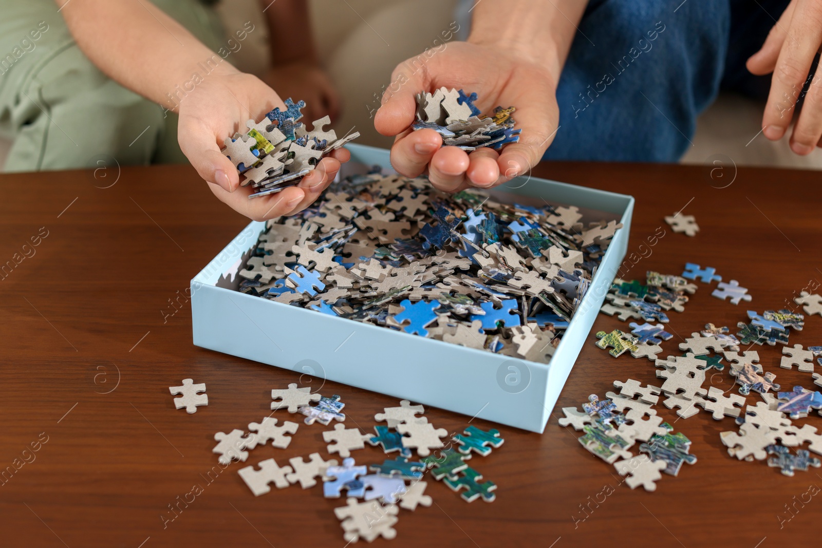 Photo of Father and his daughter with box of puzzle pieces at wooden table, closeup