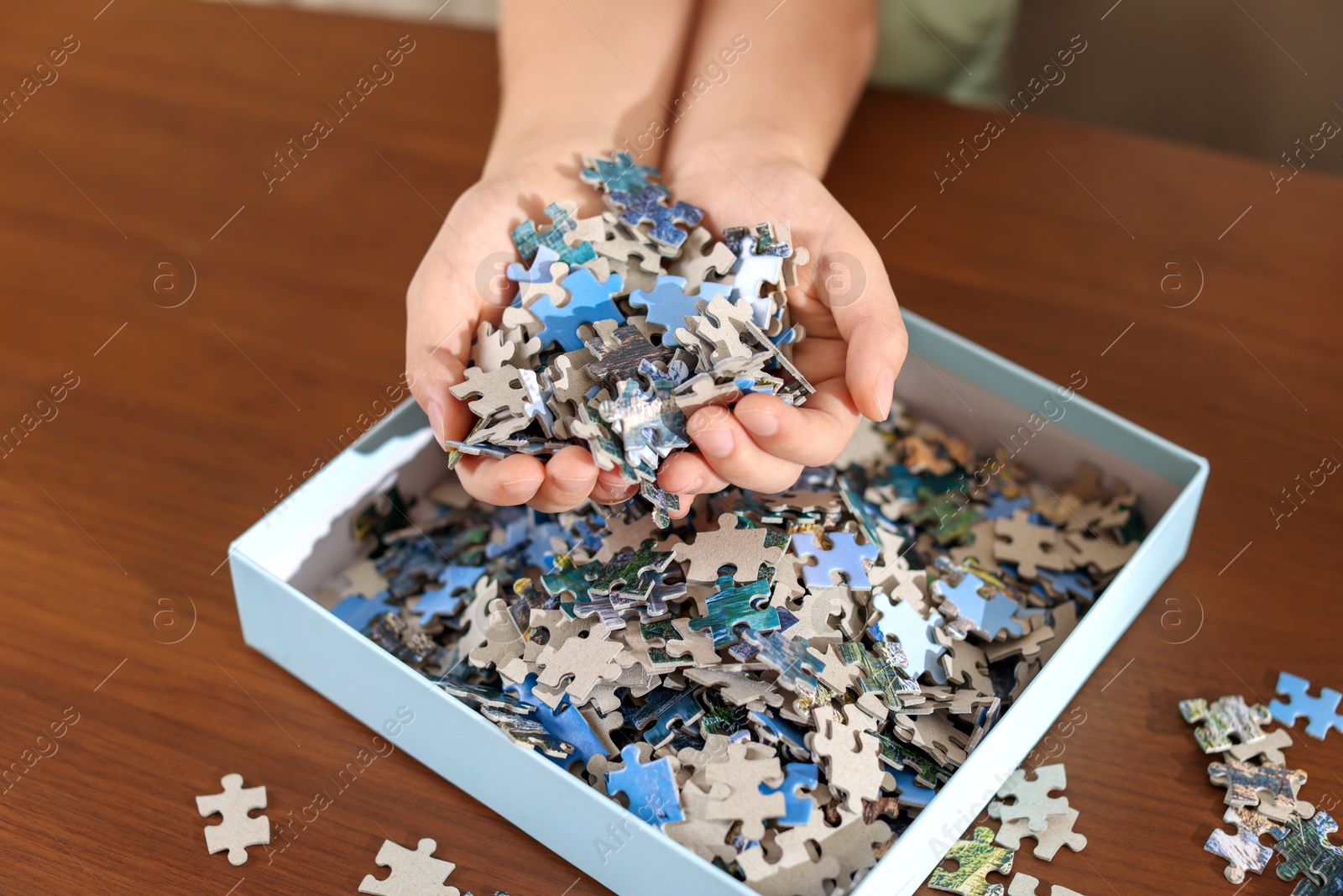 Photo of Girl with box of puzzle pieces at wooden table, closeup