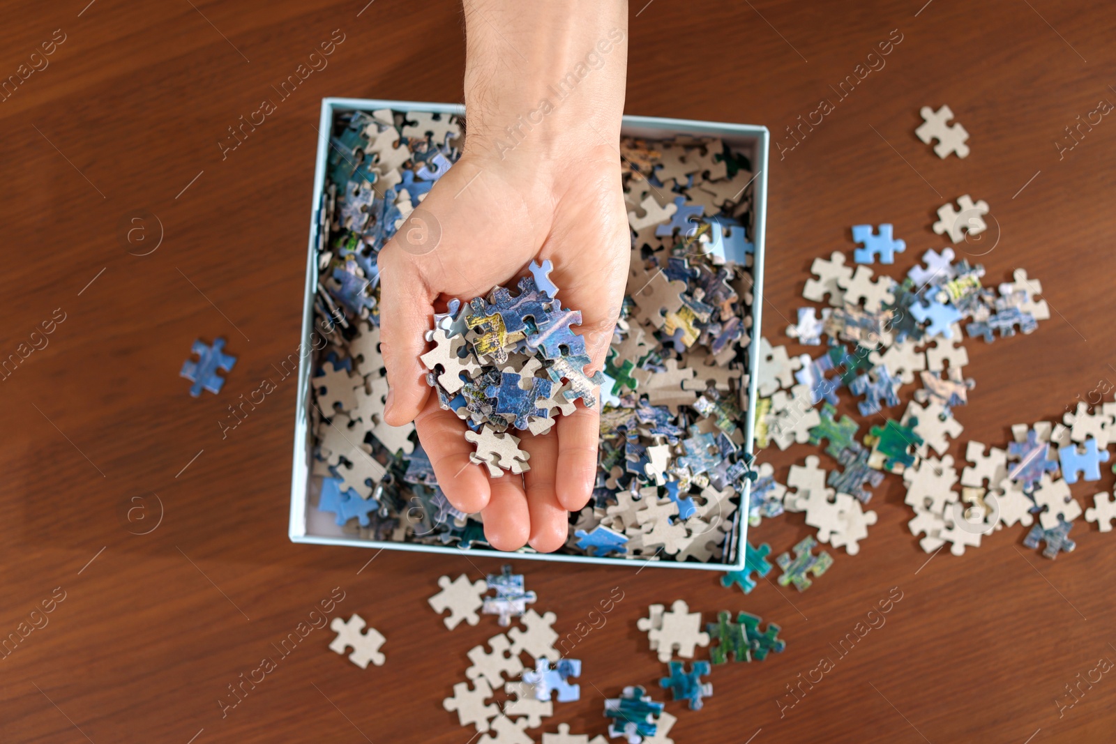 Photo of Man with box of puzzle pieces at wooden table, top view