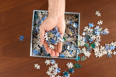 Photo of Man with box of puzzle pieces at wooden table, top view