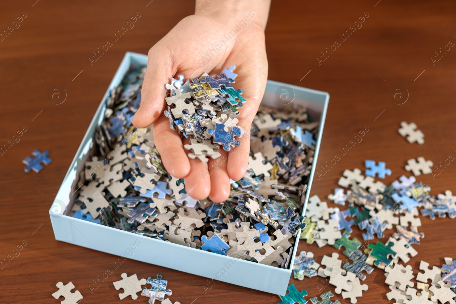 Photo of Man with box of puzzle pieces at wooden table, closeup