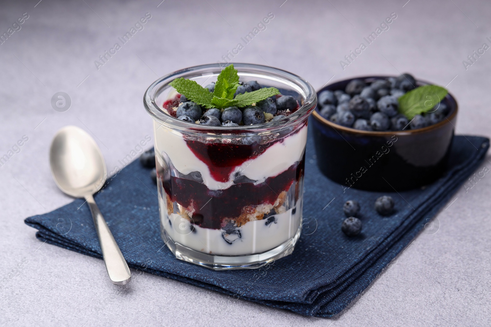 Photo of Tasty trifle dessert. Blueberries, sponge cake and whipped cream in glass on light grey table