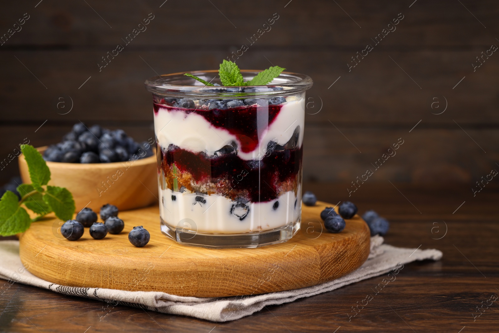 Photo of Tasty trifle dessert. Blueberries, sponge cake and whipped cream in glass on wooden table, space for text