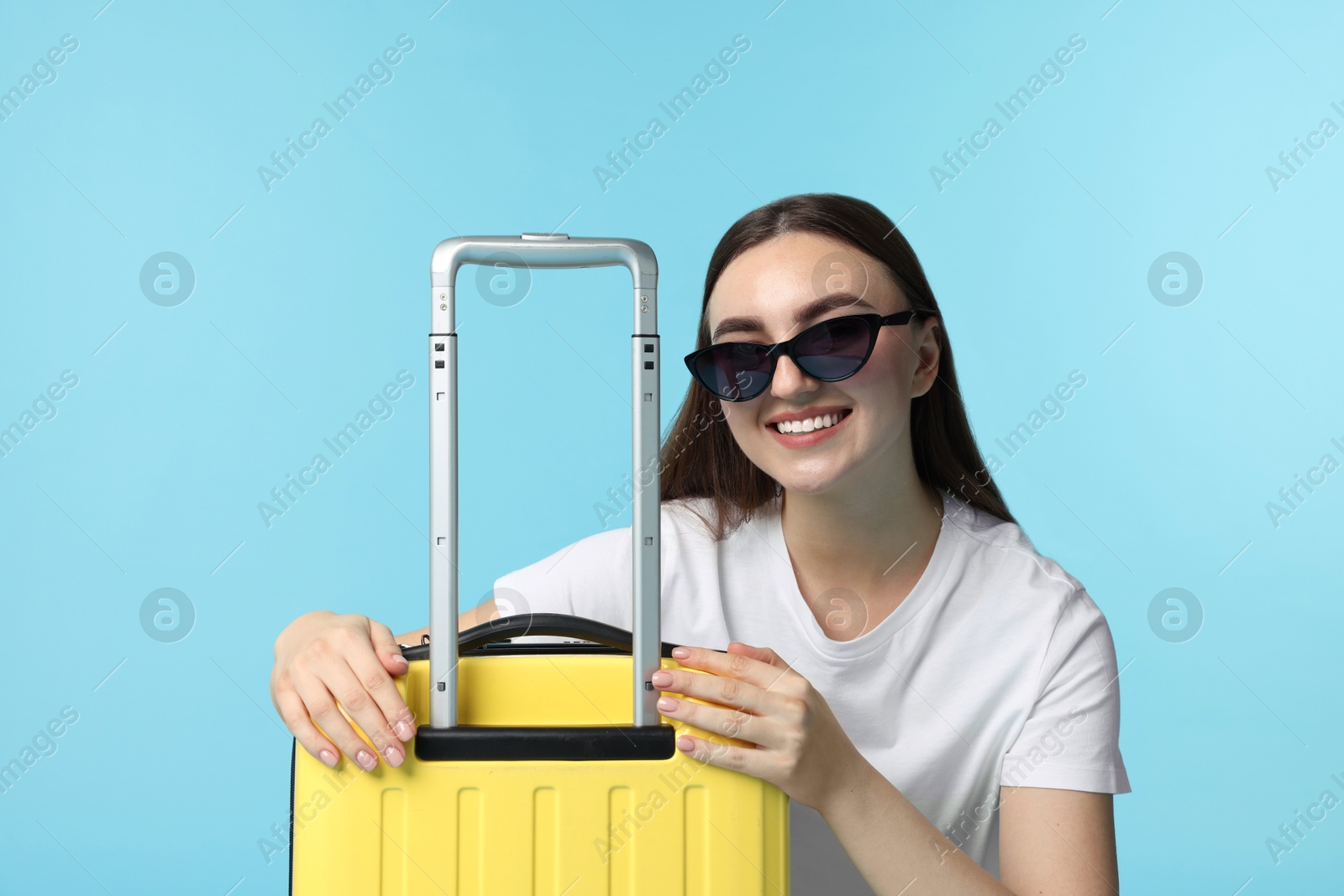 Photo of Woman with suitcase wearing sunglasses on light blue background