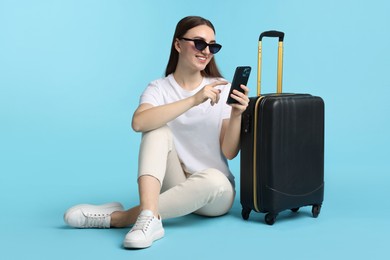 Photo of Woman with suitcase and smartphone on light blue background