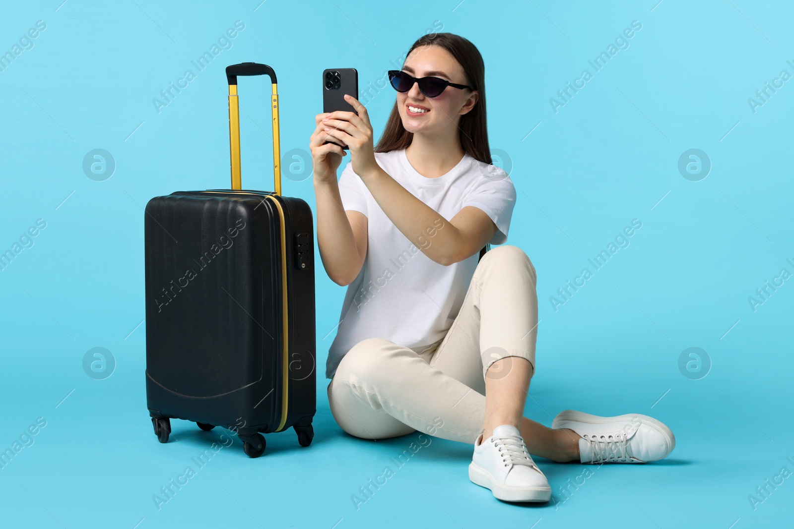 Photo of Woman with suitcase taking selfie on light blue background