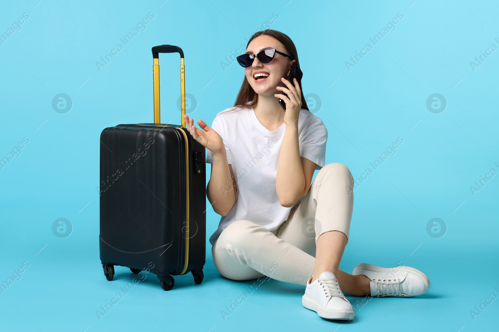 Photo of Woman with suitcase talking on smartphone against light blue background