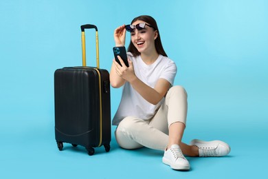 Woman with suitcase and smartphone on light blue background