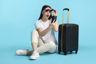 Photo of Emotional woman with suitcase and smartphone on light blue background