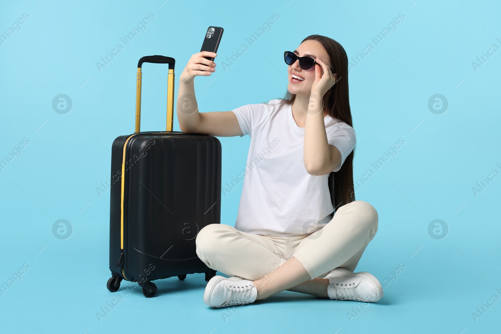 Photo of Woman with suitcase taking selfie on light blue background