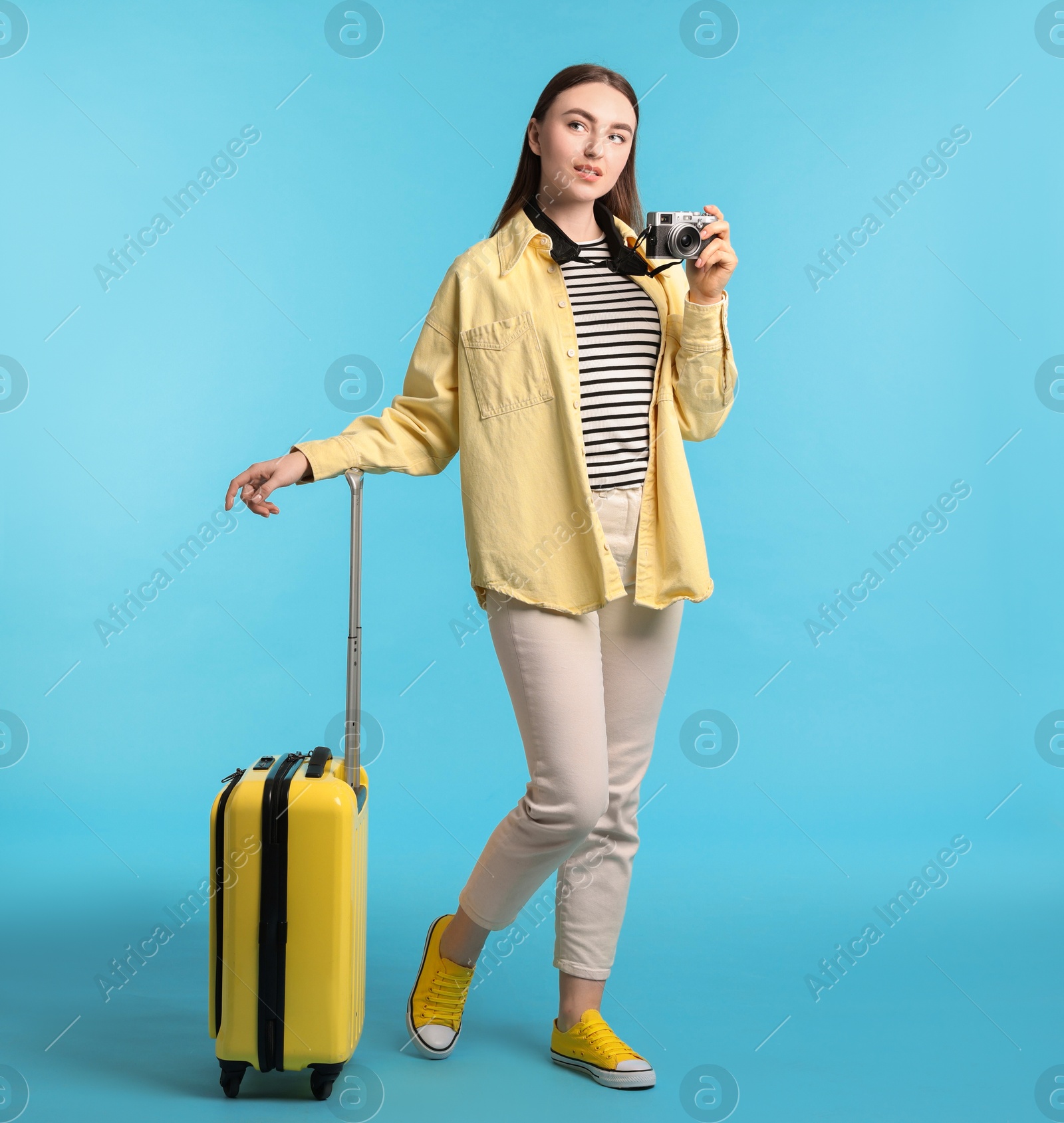 Photo of Woman with vintage camera and suitcase on light blue background