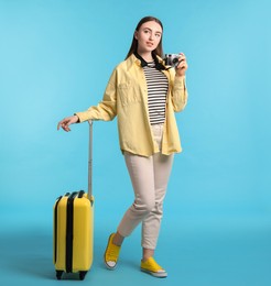 Photo of Woman with vintage camera and suitcase on light blue background