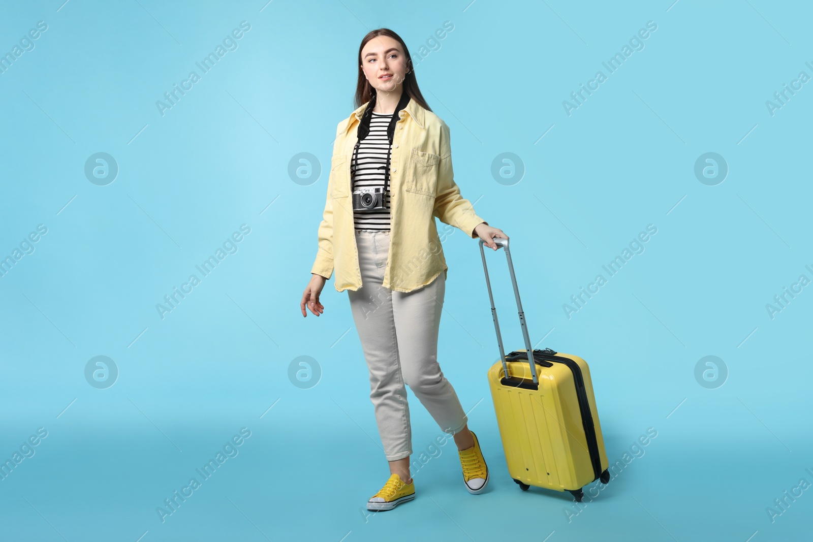 Photo of Woman with vintage camera and suitcase on light blue background