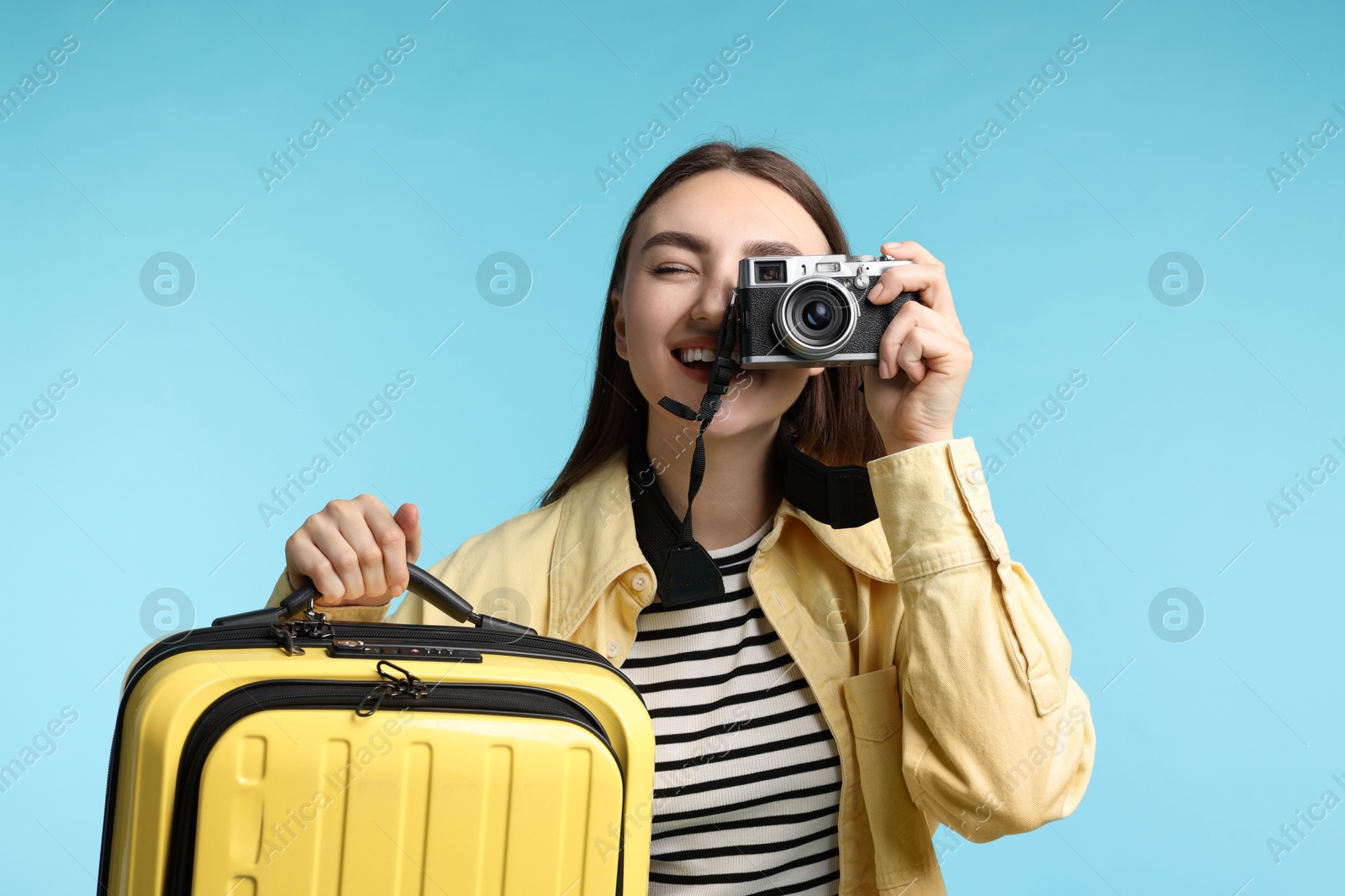 Photo of Woman with vintage camera and suitcase on light blue background