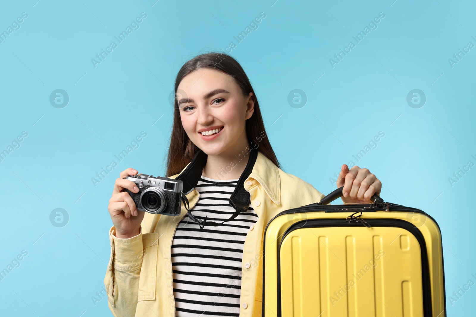 Photo of Woman with vintage camera and suitcase on light blue background