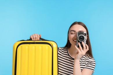 Photo of Woman with vintage camera and suitcase on light blue background