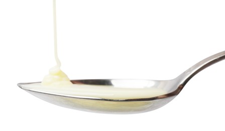 Photo of Delicious condensed milk pouring onto spoon isolated on white