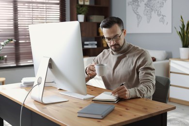 Handsome man working with computer at desk indoors. Home office