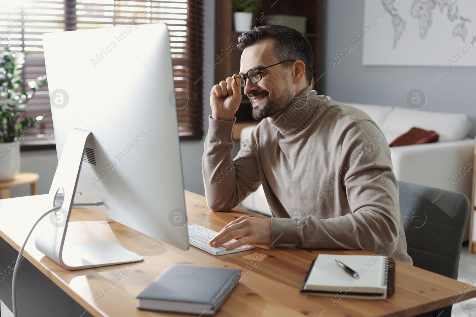 Photo of Happy man working with computer at desk indoors. Home office