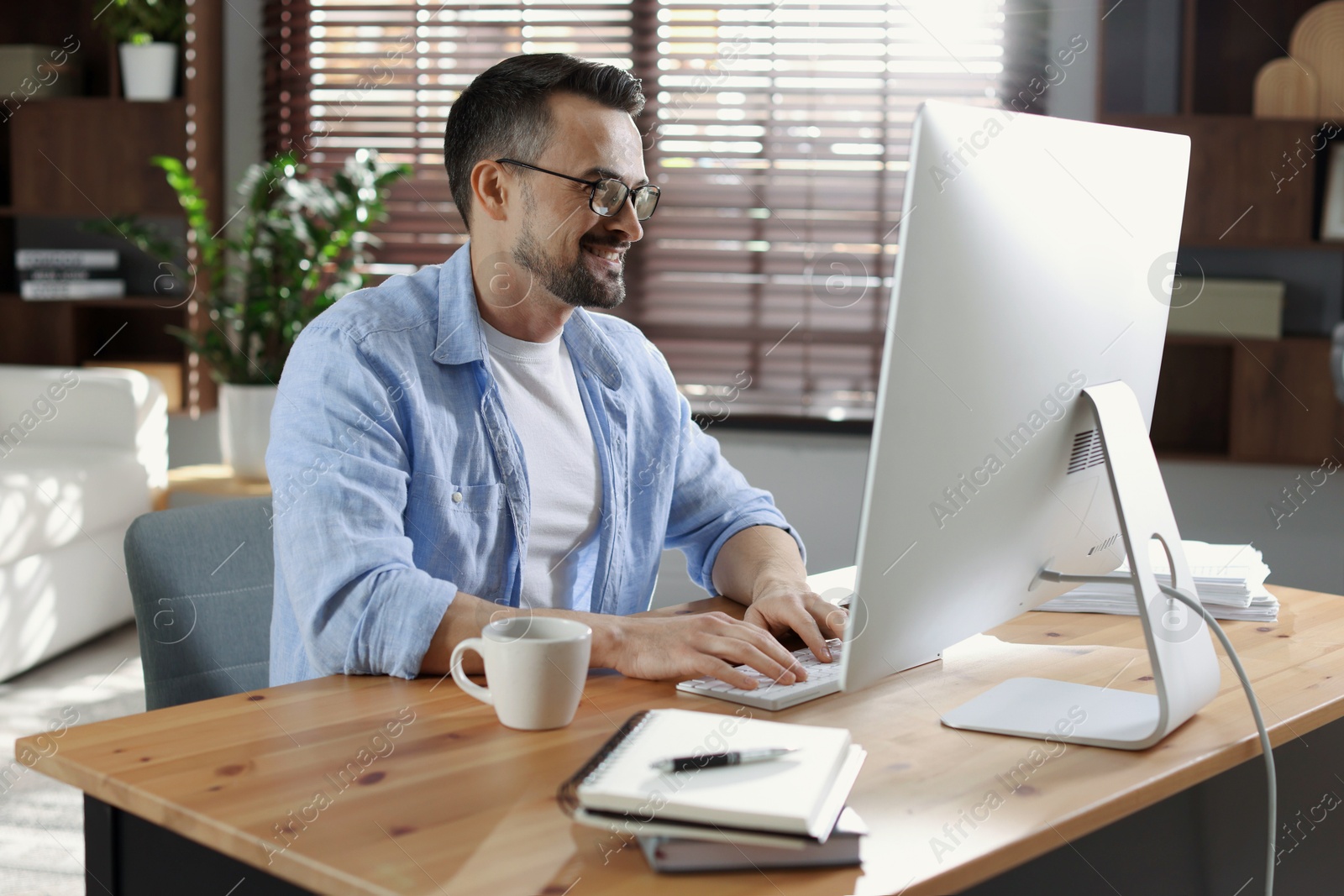 Photo of Happy man working with computer at desk indoors. Home office