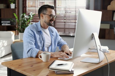 Happy man working with computer at desk indoors. Home office