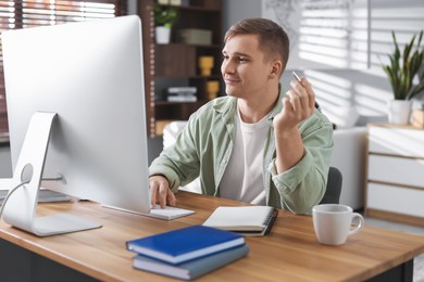 Handsome man working with computer at desk indoors. Home office