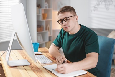 Handsome man working with computer at desk indoors. Home office