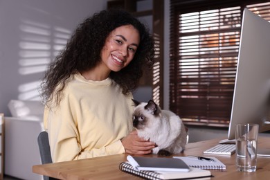 Photo of Beautiful woman with her cute cat working on computer at desk in home office