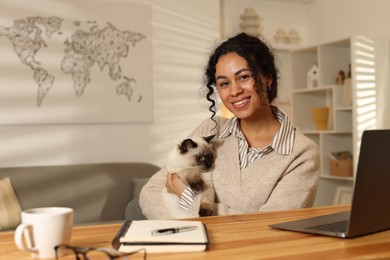 Photo of Beautiful woman with her cute cat working on laptop at desk in home office