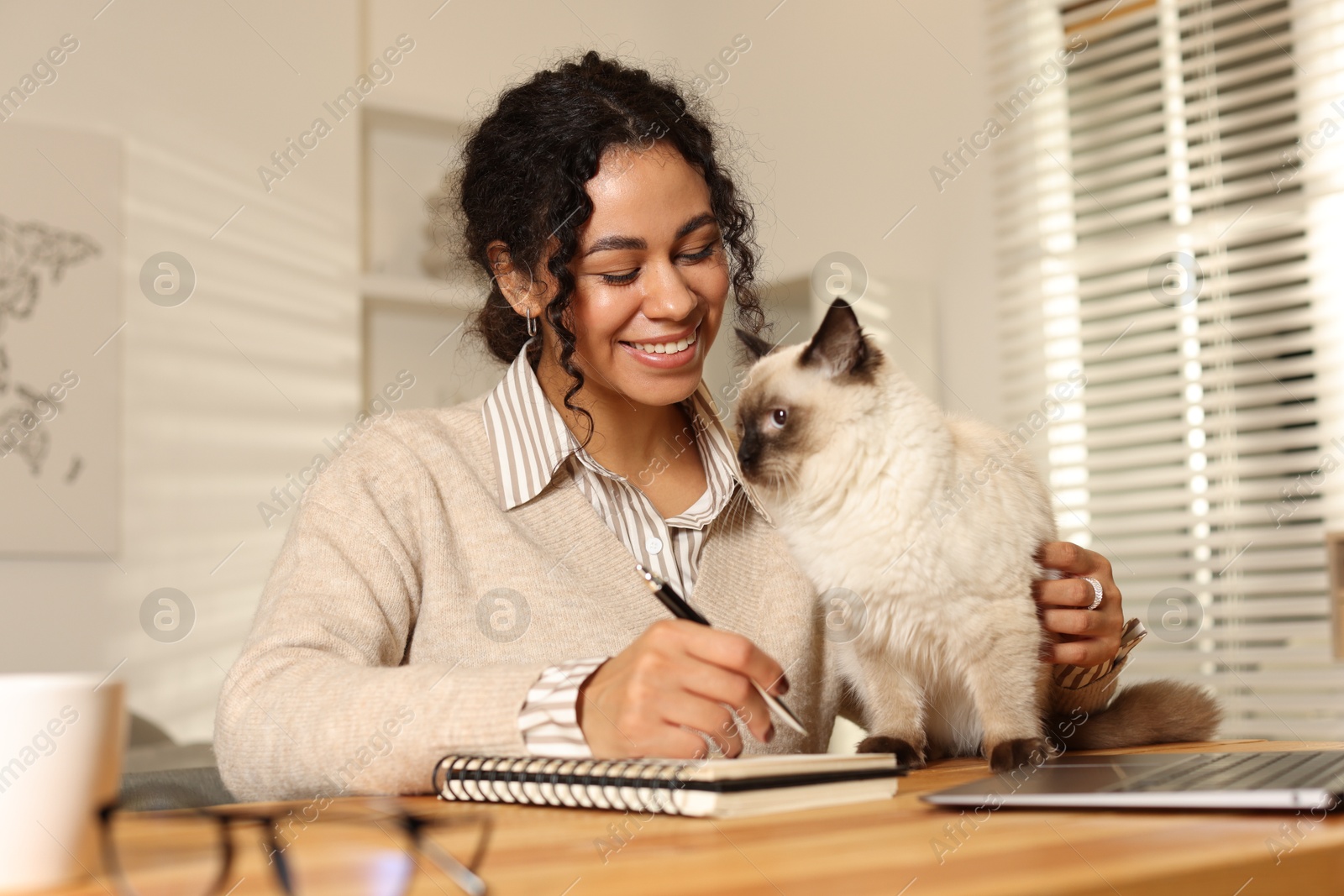 Photo of Beautiful woman with her cute cat working on laptop at desk in home office