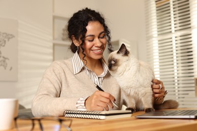 Beautiful woman with her cute cat working on laptop at desk in home office