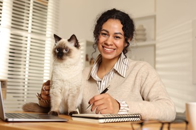 Photo of Beautiful woman with her cute cat working on laptop at desk in home office