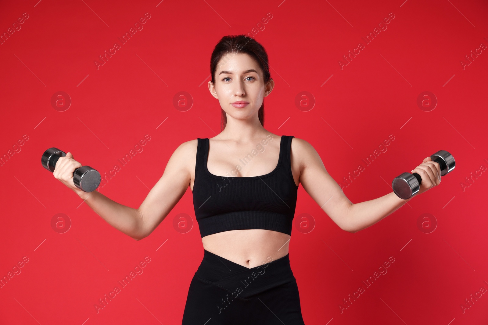 Photo of Woman in sportswear exercising with dumbbells on red background