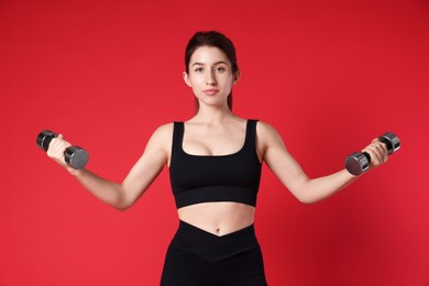 Woman in sportswear exercising with dumbbells on red background