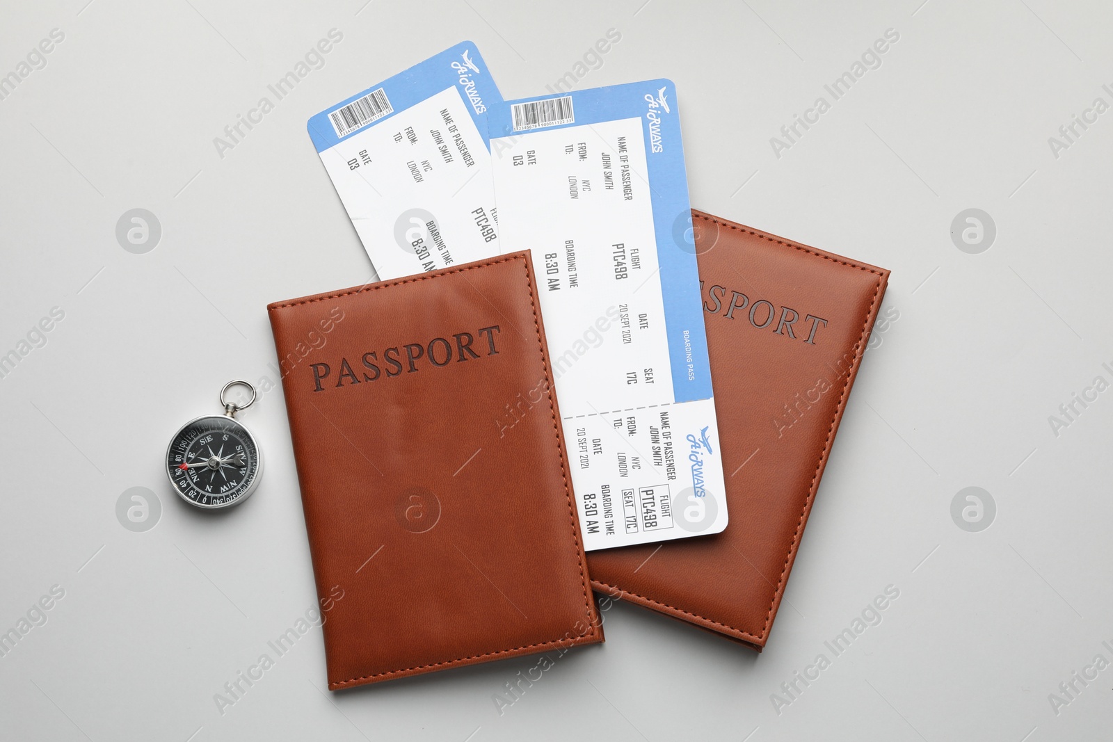 Photo of Travel agency. Flight tickets, passports and compass on grey background, flat lay