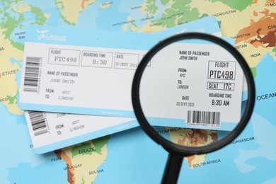 Photo of Travel agency. Looking at flight tickets through magnifying glass at world map, top view