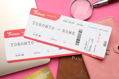 Photo of Travel agency. Flight tickets, passports, laptop and magnifying glass on pink background, flat lay