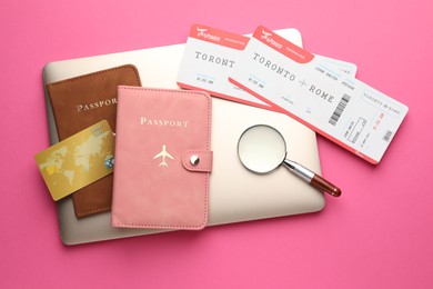 Photo of Travel agency. Flight tickets, passports, laptop, credit card and magnifying glass on pink background, flat lay