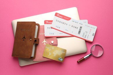 Photo of Travel agency. Flight tickets, passports, laptop, credit card and magnifying glass on pink background, flat lay